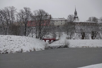 Naklejka premium Winter view to Tallinn medieval old town on Toompea hill. Snelli Toompark with red bridge over water canal. A lot of snow. Trees with no leaves. Tallinn, Estonia. January 2021