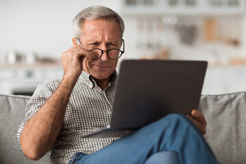 Older Male Squinting Eyes Using Laptop Wearing Eyeglasses At Home - obrazy, fototapety, plakaty