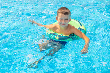 Funny happy child boy in swiming pool on inflatable rubber circle ring. Kid playing in pool. Summer holidays and vacation concept