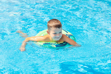 Funny happy child boy in swiming pool on inflatable rubber circle ring. Kid playing in pool. Summer holidays and vacation concept