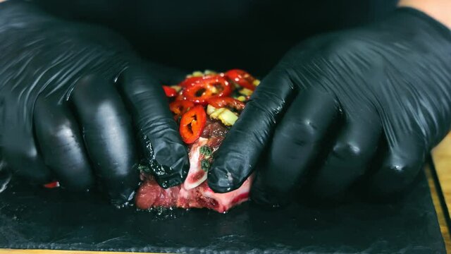cook marinates meat with vegetables. The hands of the chef in black gloves sho mix pieces of vegetables and marinade with steak. Marinating steak. The chef prepares the meat.