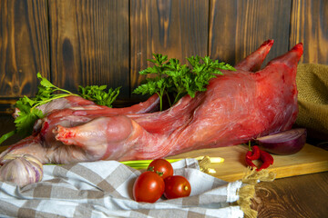 Nutria carcass on a wooden cutting board with fresh vegetables and herbs.