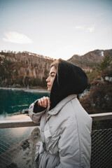 Woman tourist stands on bridge over the river. Portrait young female on mountains background, sunset in autumn day. Tourist trips to the Altai mountains, Siberia. Patmos island