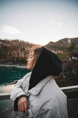 Woman tourist stands on bridge over the river. Portrait young female on mountains background, sunset in autumn day. Tourist trips to the Altai mountains, Siberia. Patmos island