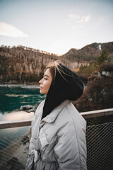 Woman tourist stands on bridge over the river. Portrait young female on mountains background, sunset in autumn day. Tourist trips to the Altai mountains, Siberia. Patmos island
