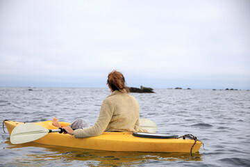 Woman kayaking in a yellow kayak around rocks in the ocean
