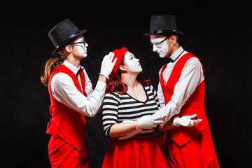 Portrait of three mime artists, isolated on black background. A man joins the heads of a man and a...