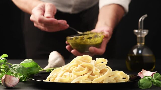 chef adds pesto genovese to pasta dish close-up on black table with ingredients