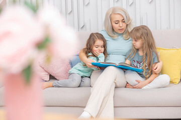 Caucasian mom reading a book to children sitting on the sofa in the living room