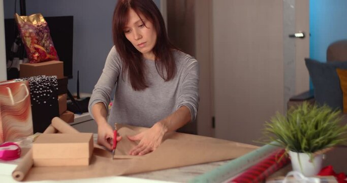 Woman Cutting Wrapping Paper and wrapping holyday gift, decorating stylish gift in craft paper on table in home