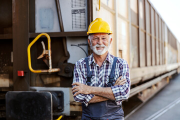 A happy, proud senior worker standing next to a wagon with arms crossed and looking at the camera....