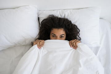 Afro american woman hides under soft white blanket