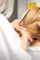 Naklejka premium Close-up hairdresser styling blonde hair on the back of the head in a beauty salon