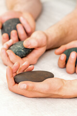 Fototapeta na wymiar Four hands of male masseurs holding spa stones on white towel top view. Stone massage concept