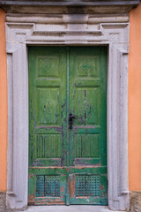 Alte gr&uuml;ne T&uuml;re mit schwarzem Griff und oranger Fassade.