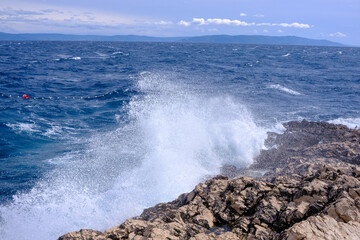 Wellen schlagen an einen Felsen und Wassertropfen fliegen durch die Luft, Gischt.