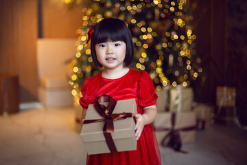 beautiful Korean child girl in red dress stands at the Christmas tree on Christmas day