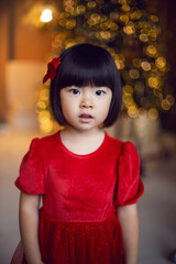 beautiful Korean child girl in red dress stands at the Christmas tree on Christmas day