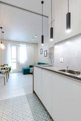 Minimalistic design of a white studio apartment. View from the entrance hall to a compact built-in kitchen, a cozy room with a sofa