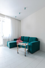 Minimalistic interior design studio apartment with white walls and a turquoise green sofa. Living room and dining room for a comfortable life