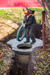 A worker installs a sewer manhole on a septic tank made of concrete rings. Construction of sewage disposal systems for private houses