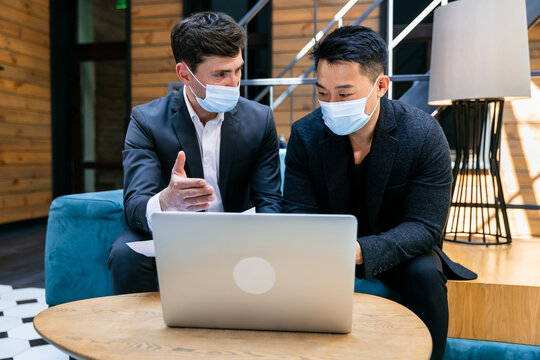 men sit on the couch, meet discussing joint business at a laptop computer wearing a face mask prevent pandemic coronavirus