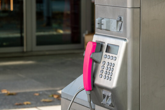 Public telephone made of silver metal with pink telephone receiver