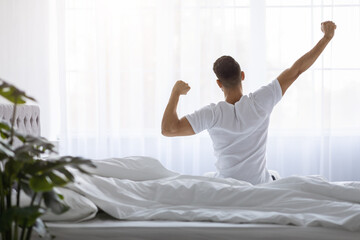Man Stretching In Bed After Waking Up In The Morning, Rear View - obrazy, fototapety, plakaty