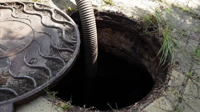 An open manhole in the courtyard of a private house . Image of the nodes of the pumping machine for pumping out the septic tank. pumping waste from the sewer. A hose is lowered into the sewer