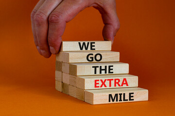 We go the extra mile symbol. Wooden blocks with words We go the extra mile. Beautiful orange background, copy space. Businessman hand. Business, we go the extra mile concept.