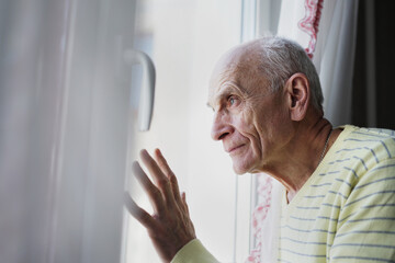 Mature person looking through window with white curtain at home