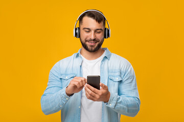 Happy middle aged european man in headphones switches song in app in smartphone
