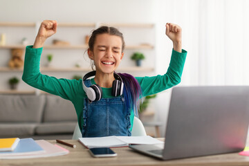 Portrait of emotional girl shaking fists using laptop pc