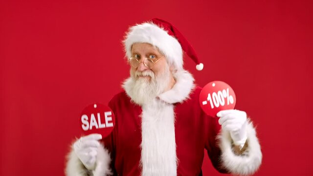 Christmas SALE -100 Off. Cheerful Santa Claus is Dancing and Joyful From Christmas Sale Holding Two Banners With Inscription SALE and -100 Off Showing Off Inscriptions to Camera on Red Background.