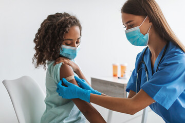 Medical Worker Vaccinating Black Pre-Adolescent Girl Making Vaccination In Clinic