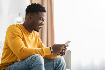 Happy black guy chatting with girlfriend, using smartphone at home - obrazy, fototapety, plakaty
