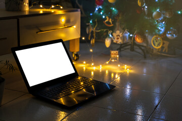 Laptop with blank screen on the floor and Christmas tree with lights in the background