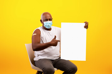 Coronavirus vaccination. Senior black man in anti covid mask with adhesive bandage pointing at...