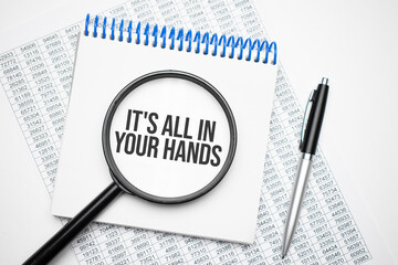 In the notebook is the text of It is all in your hands, next to the black pen, magnifying glass. A business concept.