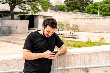 Fototapeta premium Young Latino checking the messages on his cell phone while smiling. Communications, technology concept.
