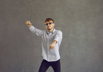 Studio portrait of happy redhead young man in thug life glasses dancing gangnam style. Cheerful guy...