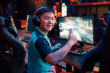 Happy male gamer showing thumb up sign and smiling while using powerful computer for online game in...