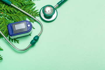 Medical concept: celebrating Christmas in healthcare. Top view of a flat lay close-up of a stethoscope, pulse oximeter with fir branches on a green background.