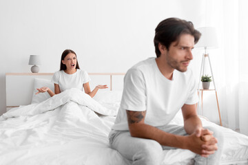 Obraz premium Unhappy frustration european young man ignoring angry woman, lady sits in bed and scream on guy in white bedroom