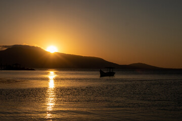 beautiful sunset overlooking the sea, in the background landscape with sun disappearing behind the mountains and yellow and orange sky