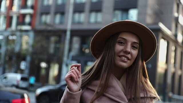 Portrait of pretty long hair young woman in a coat and round hat at the city