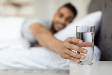 Young Arab Man Taking Glass Of Water From Bedside Table In Morning