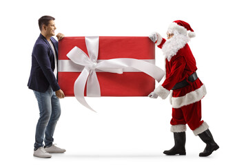 Full length profile shot of santa claus and a young man carrying a big preset