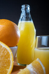 Closeup of moist oranges and glass bottle of orange juice on the table.