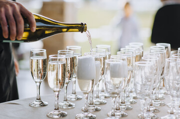 A bartender, a man pours alcohol from a bottle, champagne into glasses. Wedding photography.
